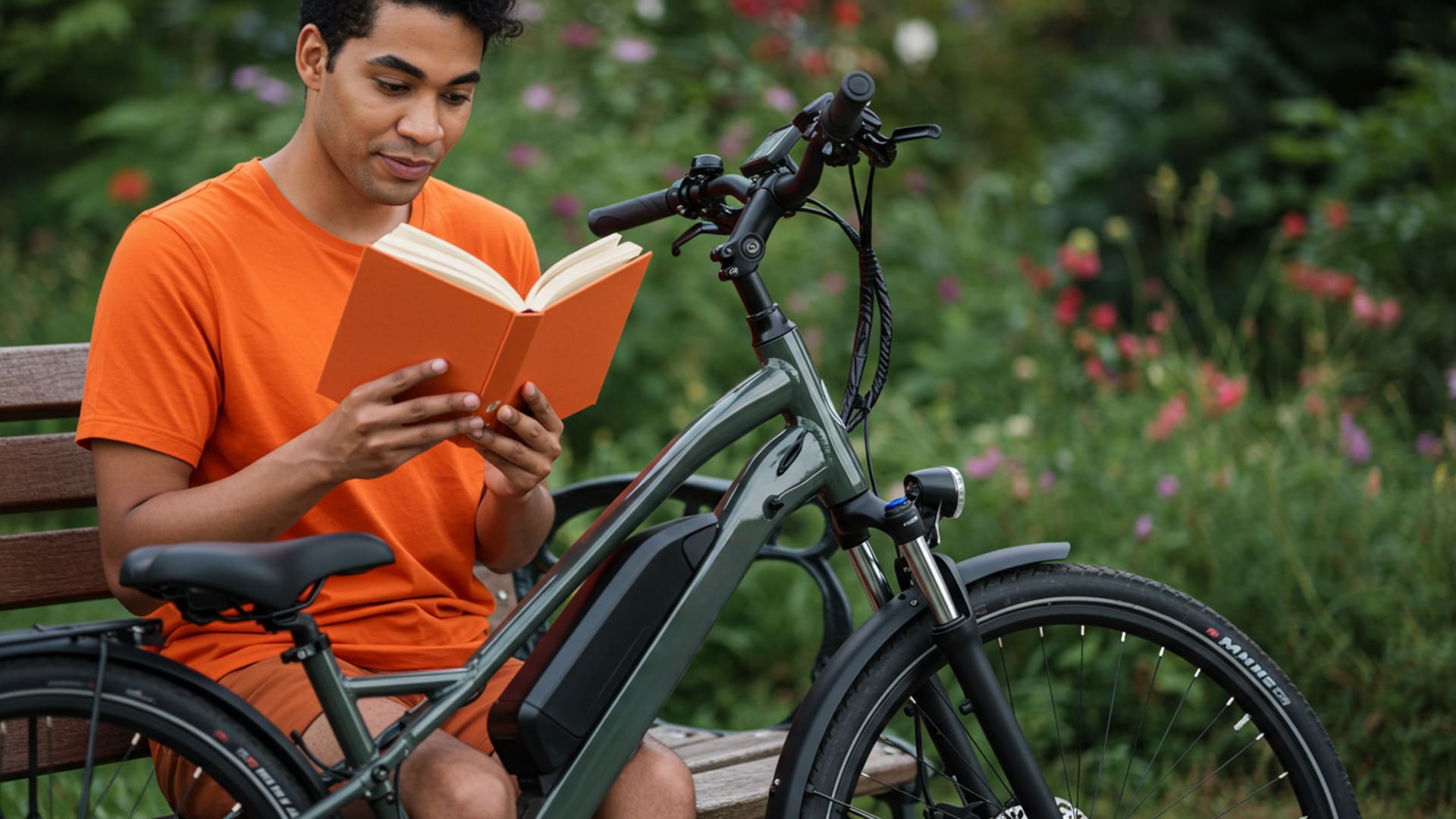 Man sitting on a bench reading a book next to his e-bike in a park